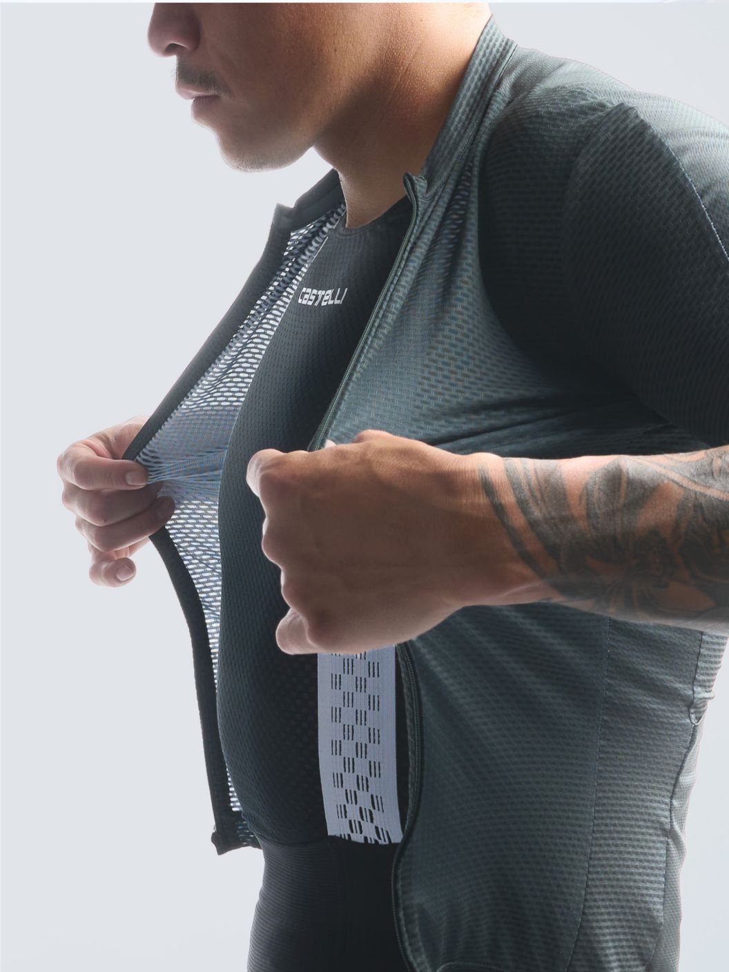 A rider pulls an unzipped jersey forward as if to zip it up to prepare for an indoor training session. 
